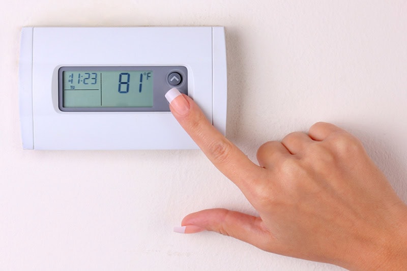 How to Set Your Programmable Thermostat. Woman changing the temperature on a thermostat.